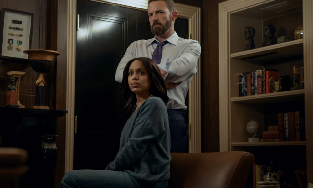 "A woman sits on a leather chair looking concerned, while a man stands behind her with arms crossed in a dimly lit office or library filled with shelves, books, and decorative objects."